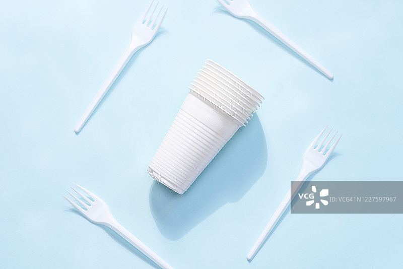 蓝色背景上的一次性塑料杯和塑料叉子。从上面看。环境污染。一次性餐具图片素材