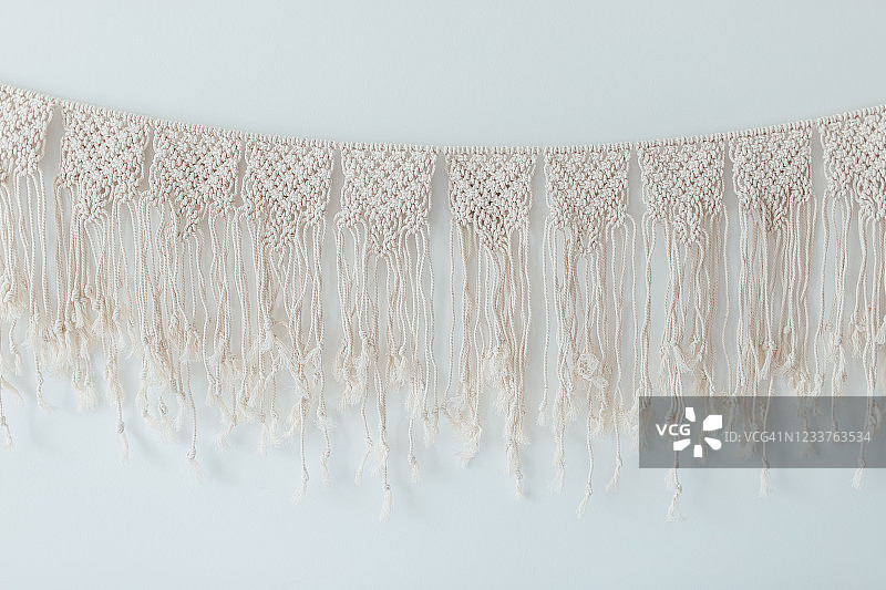一个米色100％纯棉手工macrame panno装饰挂在白色的墙壁上。设计家居装饰。波西米亚概念。图片素材