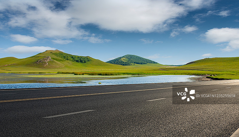 春天无尽的草原和远处沥青公路旁边的森林山丘图片素材