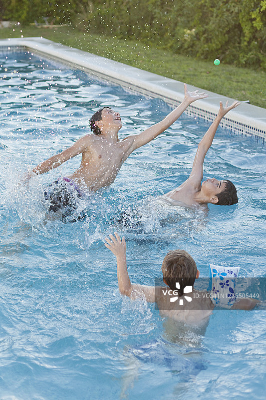 两个青少年和一个男孩在自家泳池里捡小球玩耍，水花四溅的定格画面，西班牙安达卢西亚图片素材