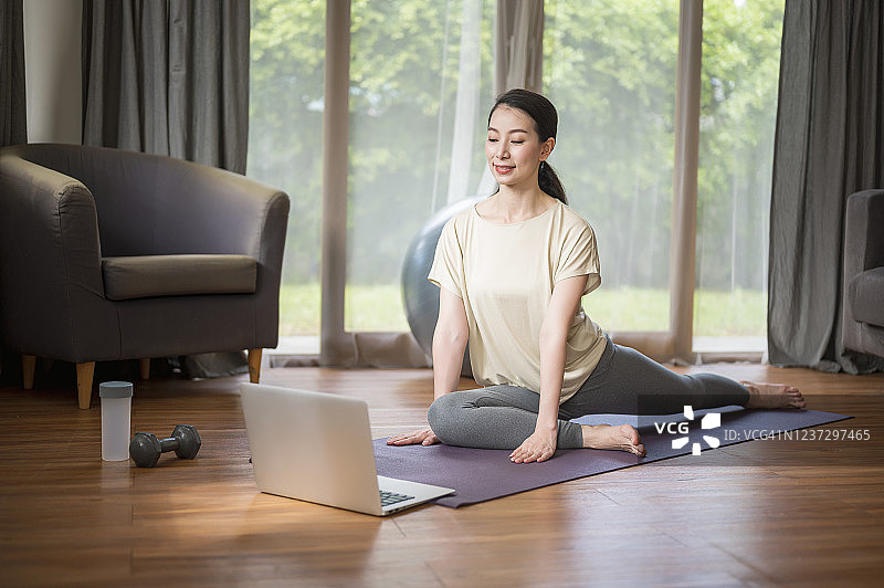 家庭锻炼教程。中年女子在家锻炼时使用笔记本电脑的镜头。健康生活方式和工作生活平衡概念。图片素材
