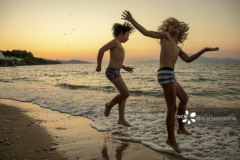 在希腊扎金索斯岛日落时跳入海中的可爱兄弟图片素材