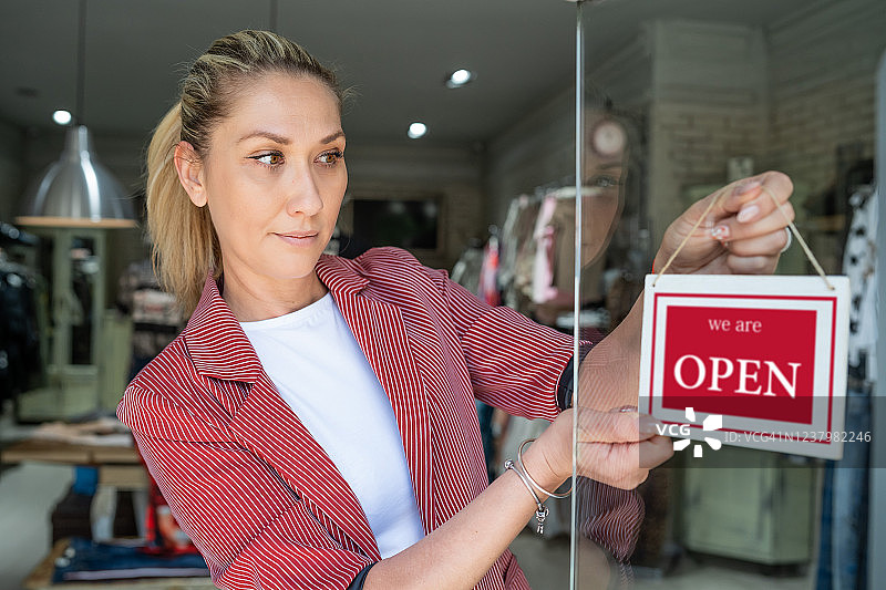 快乐的店主在门上挂着开业标志图片素材