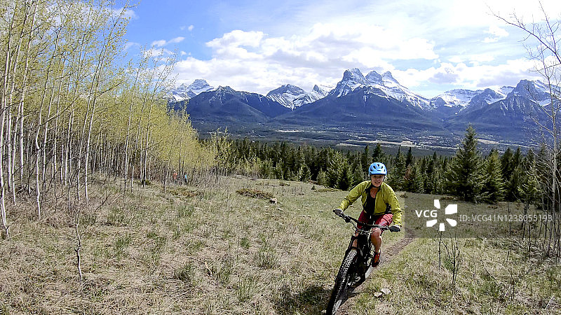 女人骑电动山地车沿着高山草甸陡峭狭窄的小路向上行驶图片素材
