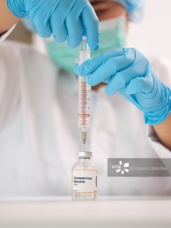戴着手套和口罩的医生，从药瓶中抽取冠状病毒疫苗图片素材