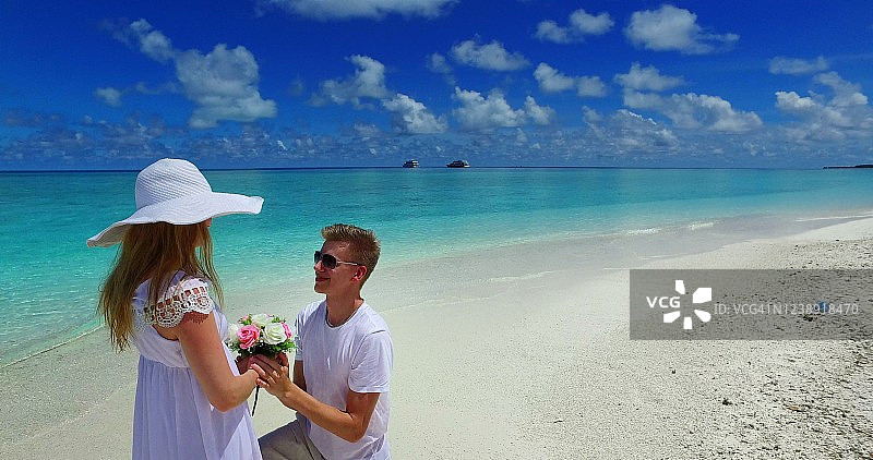 热带海岛浪漫风景中，身穿白色连衣裙的年轻男子向心爱的女友求婚，蜜月度假概念图片素材