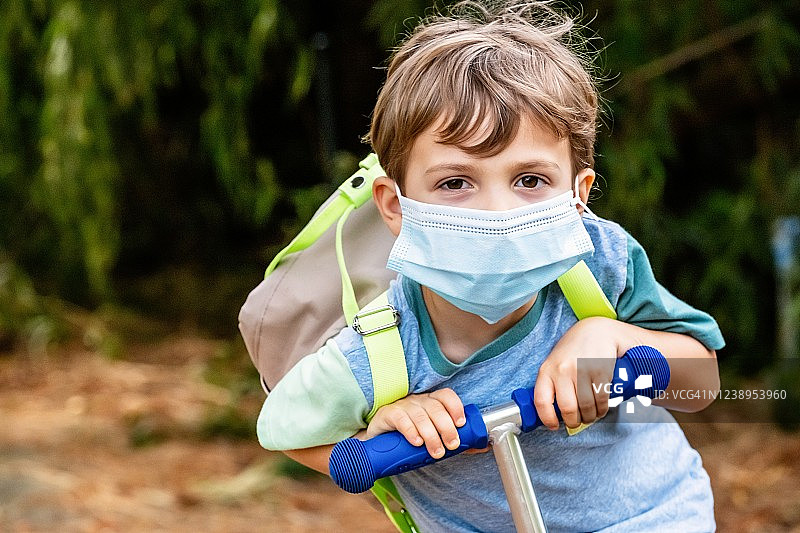 小男孩戴着防护口罩，背着背包骑滑板车图片素材