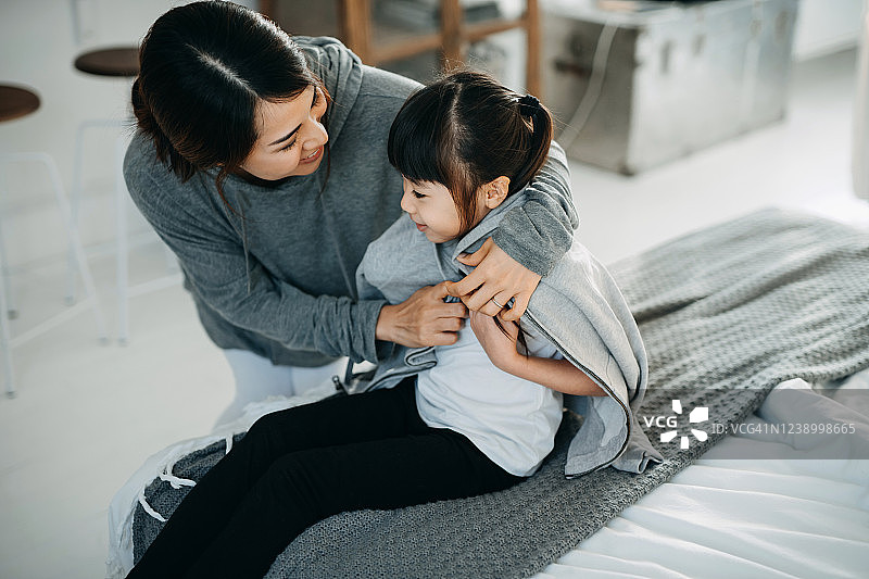 有爱心的年轻亚洲母亲在家为女儿穿外套图片素材