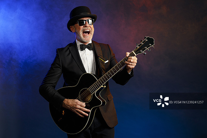 演奏吉他的英俊老年音乐家。蓝色背景，带有光线和特效烟雾图片素材
