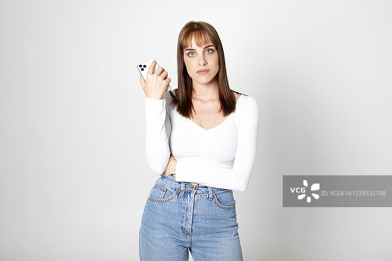 在白色背景工作室里拿着手机的漂亮女孩图片素材