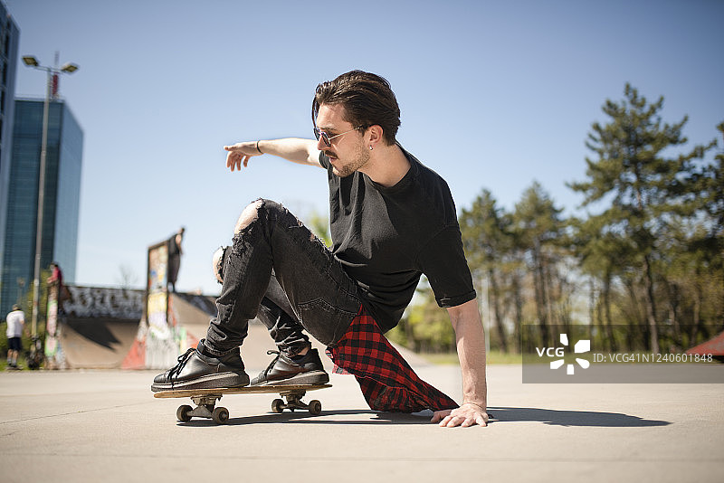 戴墨镜的时尚男人在城市滑板公园休闲图片素材