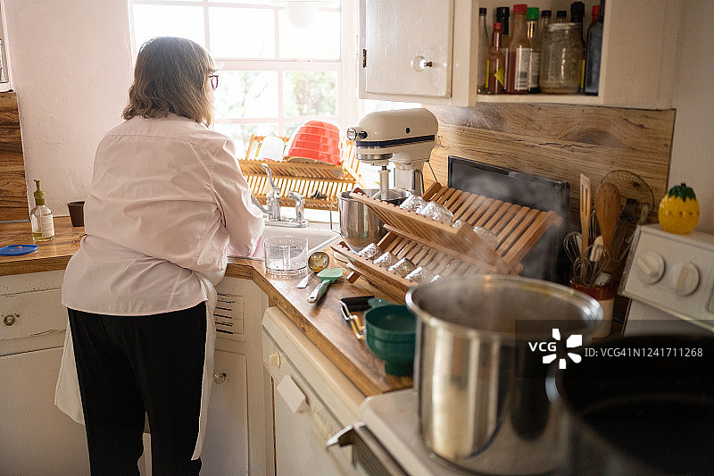 后面的年长的白人妇女在厨房做饭洗碗图片素材