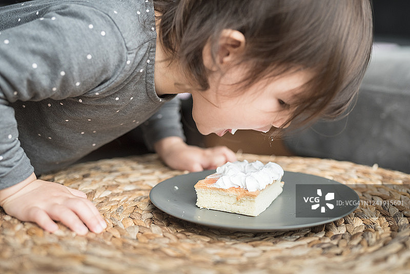 儿童在柳条桌上舔灰色盘子里海绵蛋糕上的奶油图片素材