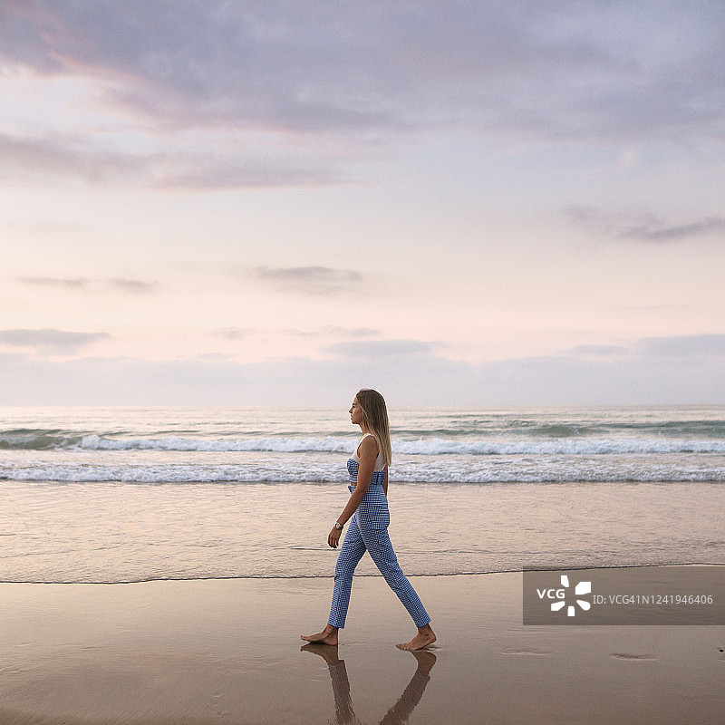 年轻女子在日落时分的海滩上散步图片素材