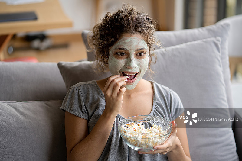 在家敷面膜、吃爆米花看电视的女人图片素材