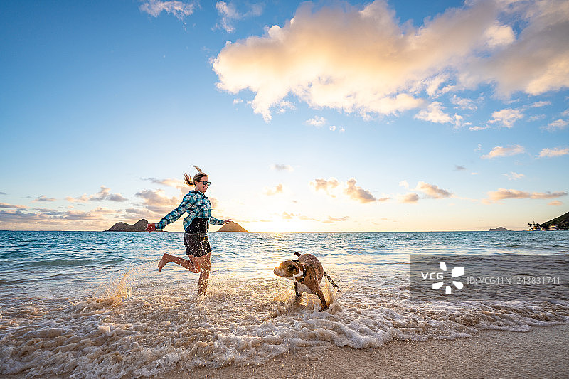 女人和拳师犬在日出时沿着海滩奔跑图片素材