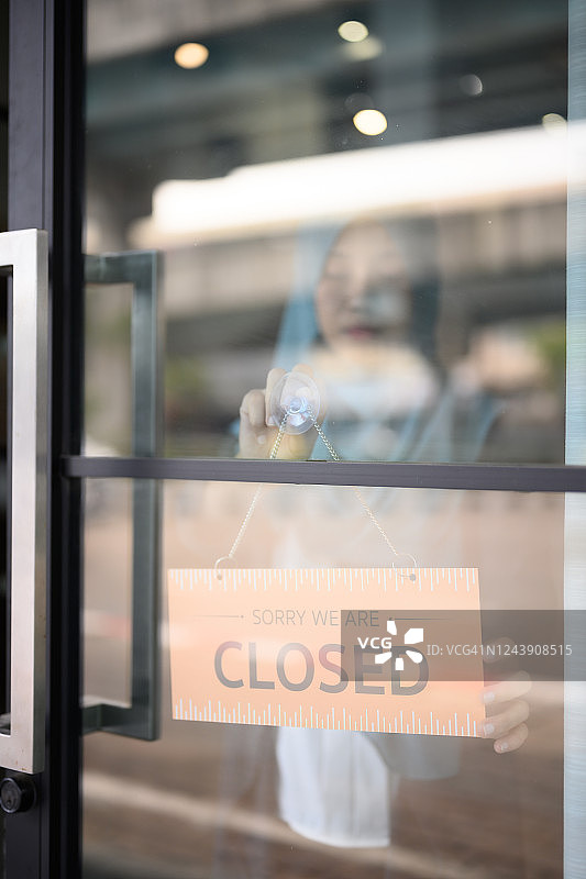 伊斯兰女人在玻璃门挂“已关门”牌图片素材