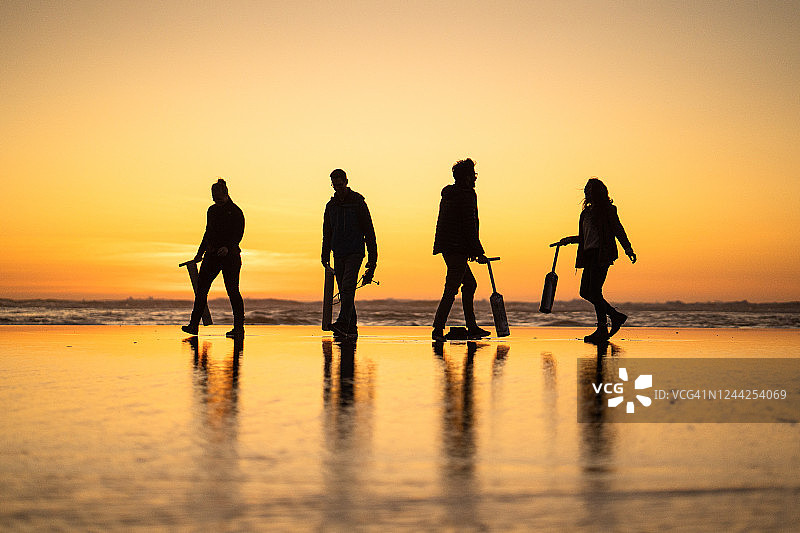 朋友们在日出时分于海滩上寻找蛤蜊图片素材