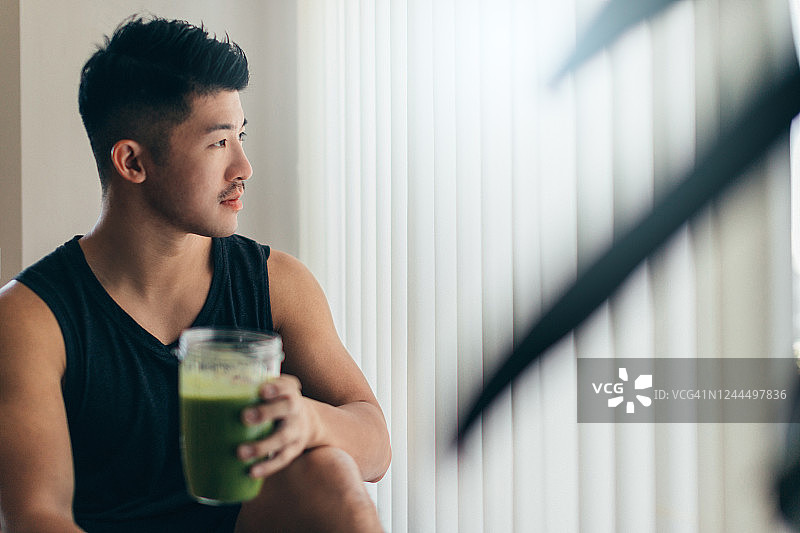 自信的亚洲男人在锻炼后喝蛋白奶昔图片素材