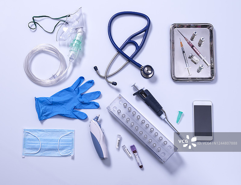 结束封锁概念，灰色背景上的医疗设备，氧气面罩，听诊器，带有接触者追踪App的手机，疫苗注射器，蓝色手套和数字温度计图片素材