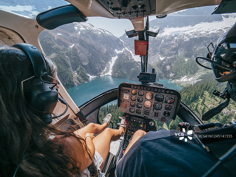 从直升机驾驶舱看到的年轻男女飞越冰川山湖的景象图片素材