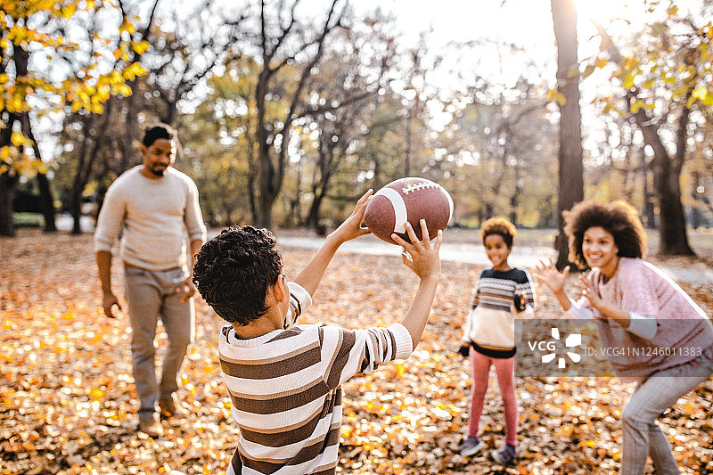 在公园里和家人一起玩橄榄球的小黑男孩的背影图片素材