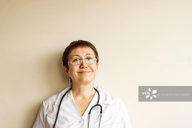 疲惫的微笑漂亮的中年女医生，带着听诊器，背景是白色的墙壁图片素材