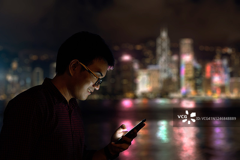 在金融区夜晚使用平板电脑，背景是灯火通明的企业摩天大楼的年轻商人图片素材