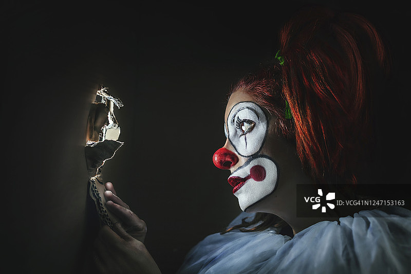 小丑从纸箱的洞里窥视，概念摄影图片素材