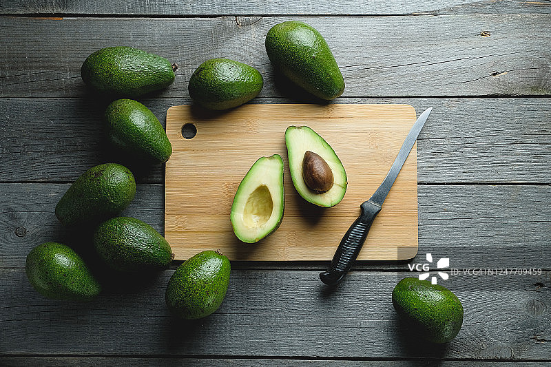 砧板上切成两半的牛油果，旁边放着整个水果和一把刀图片素材