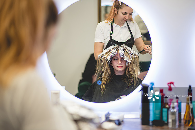 新冠疫情后重开的理发店里正在挑染头发的年轻女孩图片素材
