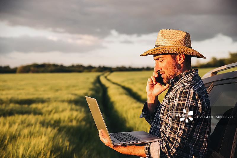 现代农民使用笔记本电脑和智能手机控制田地里的收成图片素材