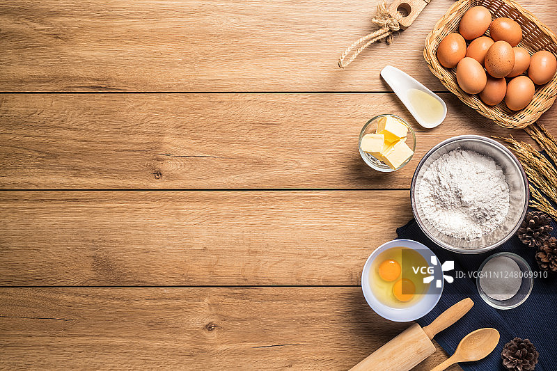 制作蛋糕的配料照片，如鸡蛋、面粉、糖、黄油、粉末和设备，在木地板上，俯视，有复制空间图片素材