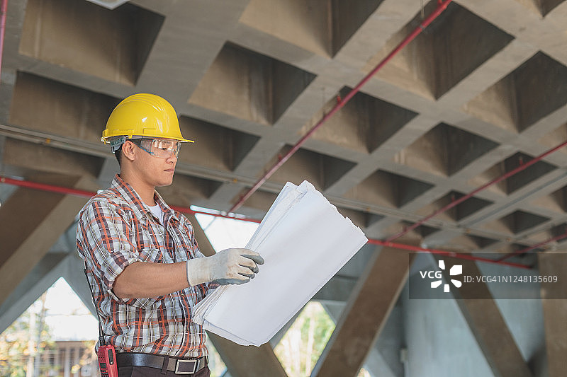 戴着安全帽的亚洲建筑工程师在建筑工地查看蓝图，工程师在现场检查建筑项目图片素材