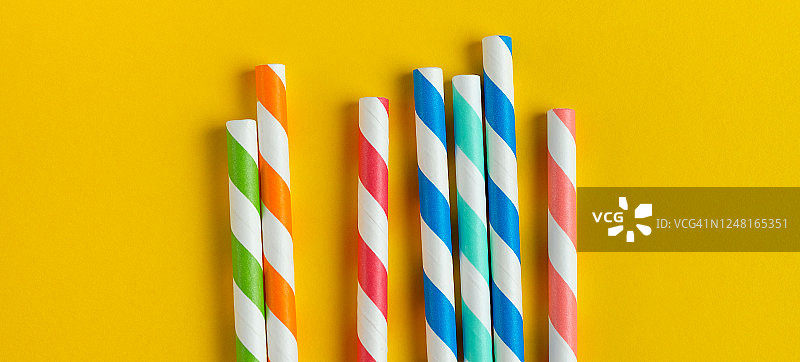 黄色背景上的彩色可重复使用条纹纸吸管（饮用果汁或鸡尾酒）图片素材