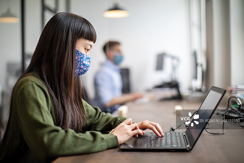 戴着口罩在办公桌前工作的女人图片素材