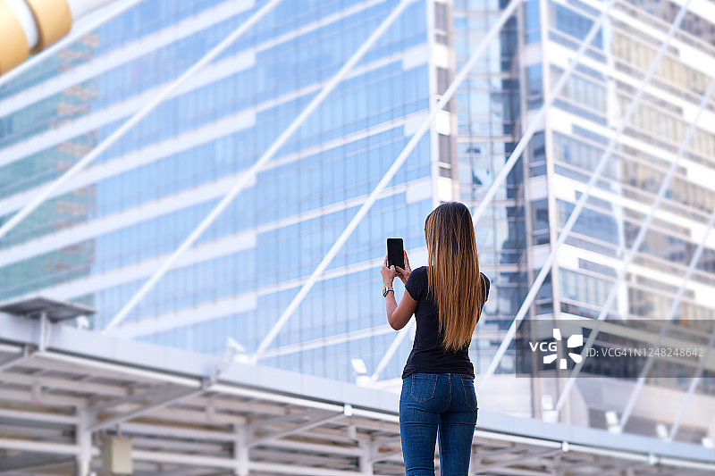 女子用手机拍摄摩天大楼的背影图片素材