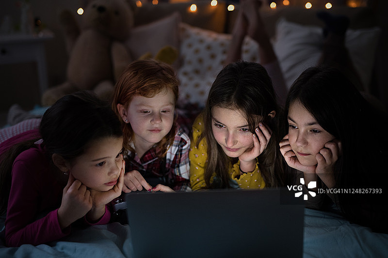 一群小女孩晚上在床上用笔记本电脑看电影图片素材