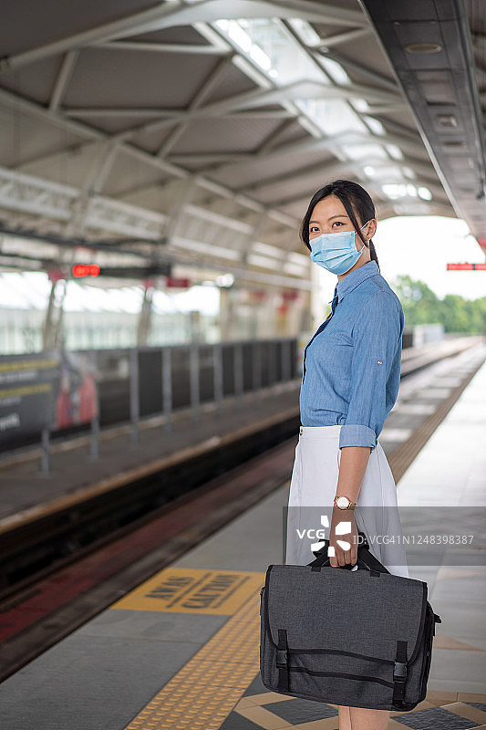 戴口罩的年轻亚洲女性在站台上等候轻轨图片素材