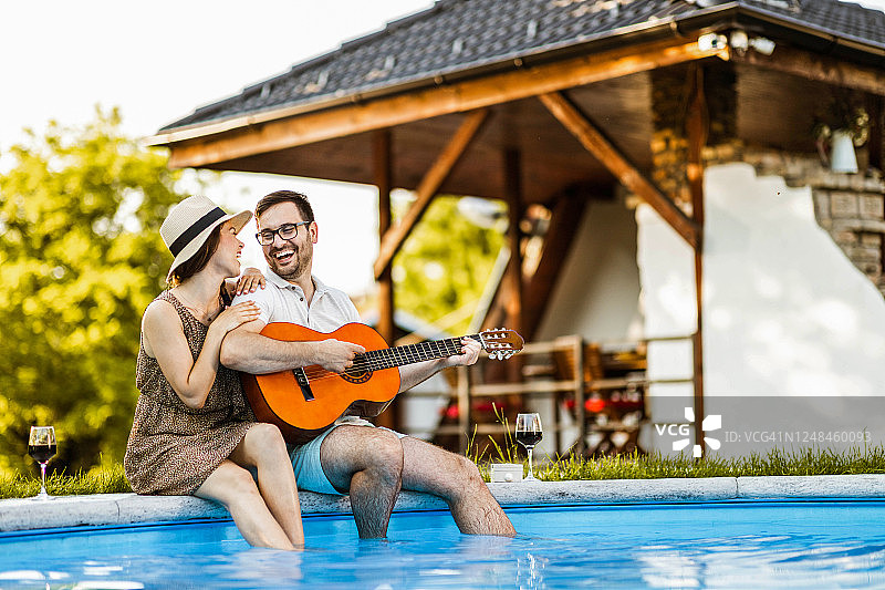 快乐的男人在泳池边为他的女朋友弹吉他图片素材