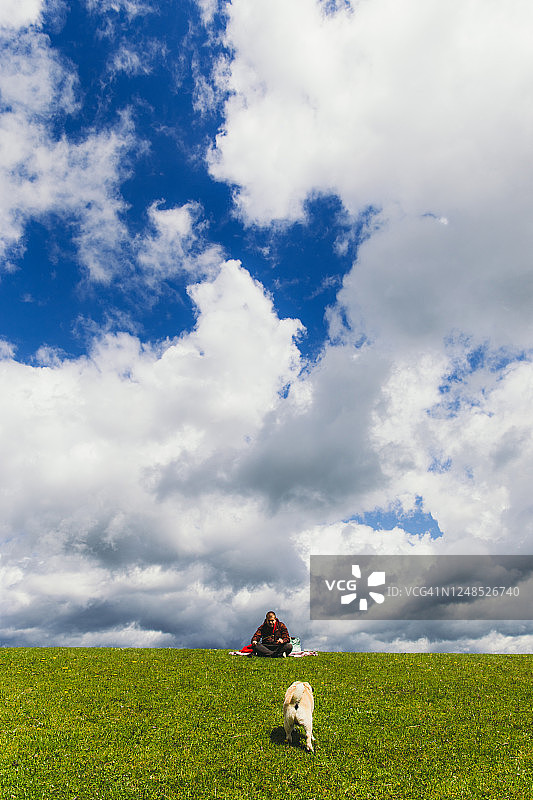 男人在美丽云空下风景如画的春日草地上与狗放松图片素材