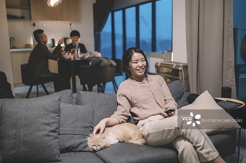 中国少女和宠物在沙发上看电视，妈妈和弟弟在餐厅用餐图片素材