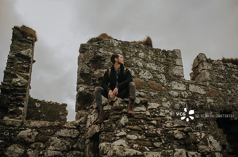 男人坐在苏格兰邓诺特城堡的废墟墙上图片素材