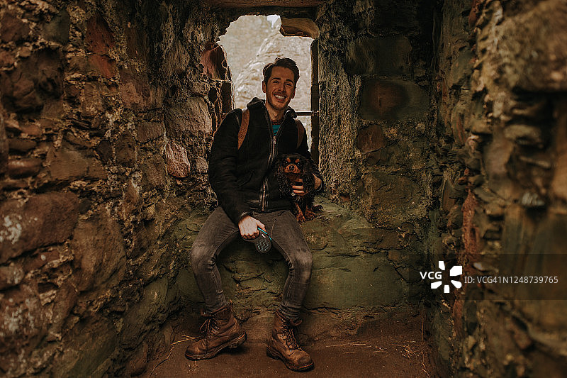 青年男子和他的狗坐在苏格兰邓诺特城堡的废墟中图片素材