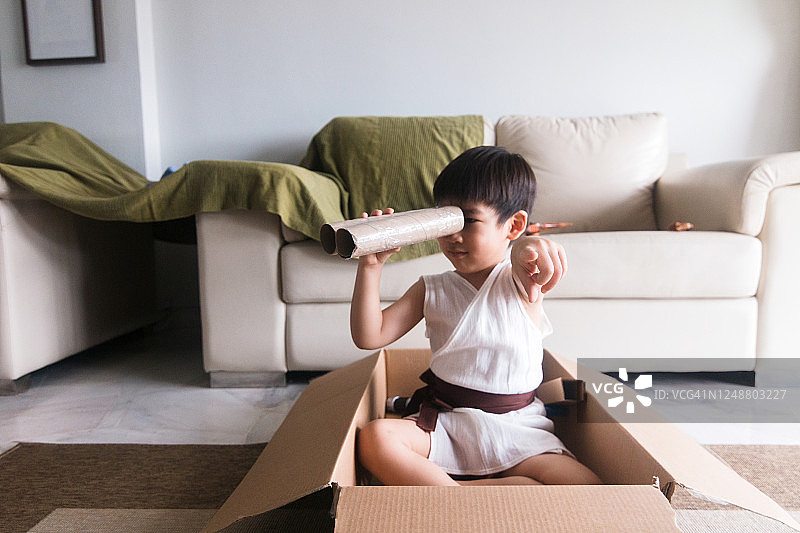 男孩在纸箱里用纸板双筒望远镜玩耍图片素材