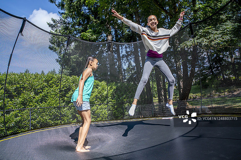 快乐的姐妹在后院的蹦床上跳跃图片素材