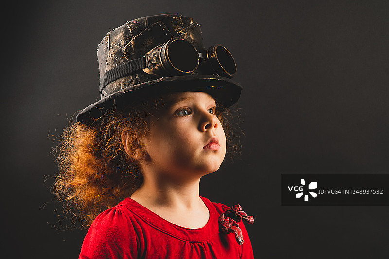 黑色背景下戴着蒸汽朋克帽子的红发卷发女孩艺术肖像图片素材