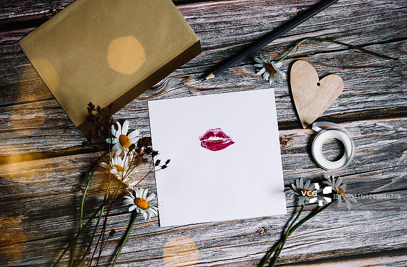 带有口红印的白纸卡片，木质背景上的雏菊花朵，夏季花卉图片素材