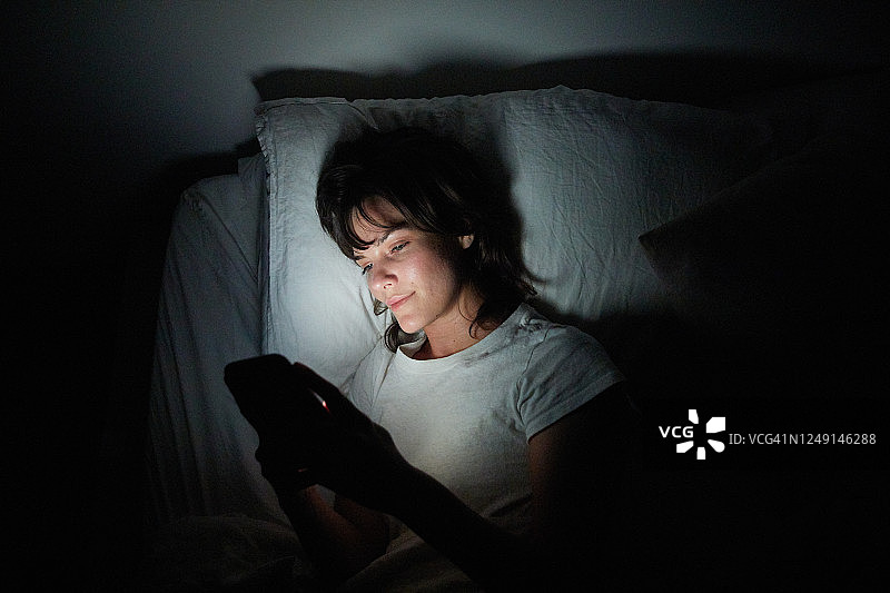 年轻女人夜晚在床上使用手机图片素材