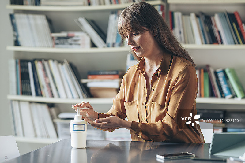 病毒预防：商务女士在工作场所使用免洗消毒凝胶清洁双手图片素材